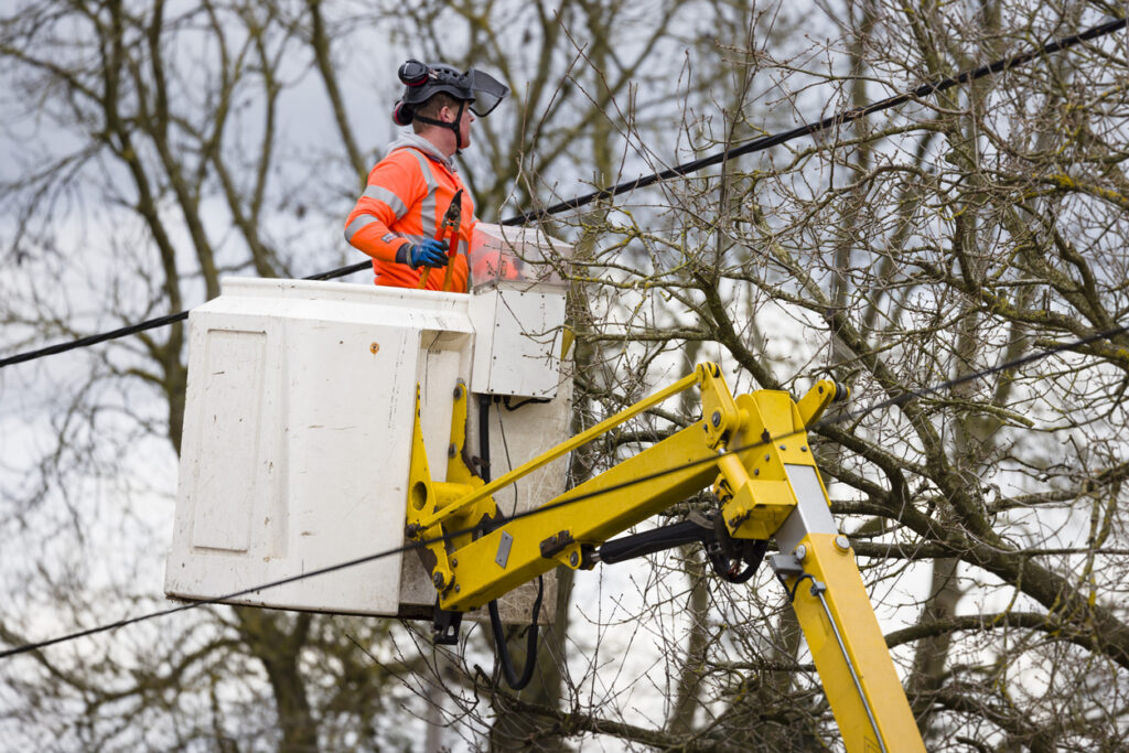 Utility worker cutting trees near overhead power lines, UK