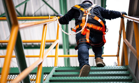 Construction worker wearing a work harness going up the stairs